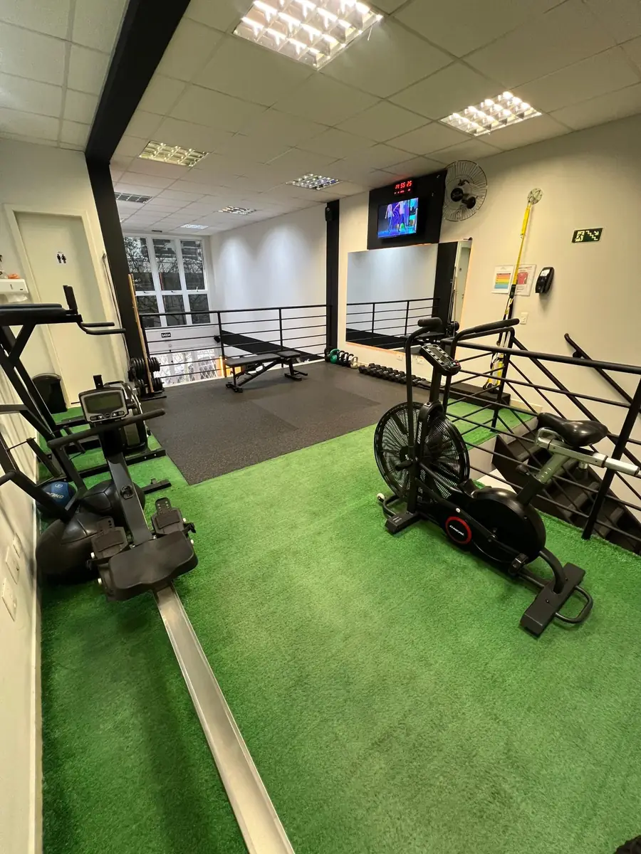 Sala de treino funcional com bikes, piso emborrachado e mezanino ao fundo.