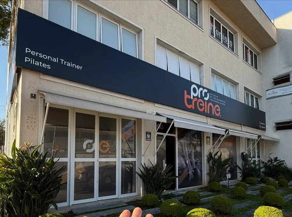 Fachada do Pro Treine, com a placa Personal Trainer e Pilates sobre as vitrines do estúdio.